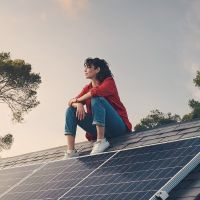 Frau sitzt auf Dach mit Photovoltaik-Anlage